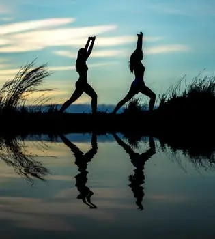 Two people doing yoga in the water at sunset.