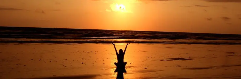A person sitting on the beach with their arms raised in front of the sun.